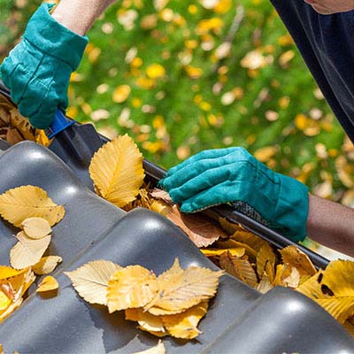 Depiction demonstrating our cleaning services by a person cleaning out clogged leaves from a seamless rain gutter.