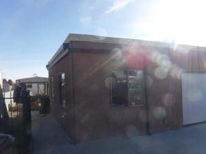 From our photo portfolio. Long brown seamless gutter wrapping around the side of a flat roof home with downspout.