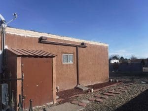 From our photo portfolio. Brown seamless gutter with downspout above a window on a flat roof house.